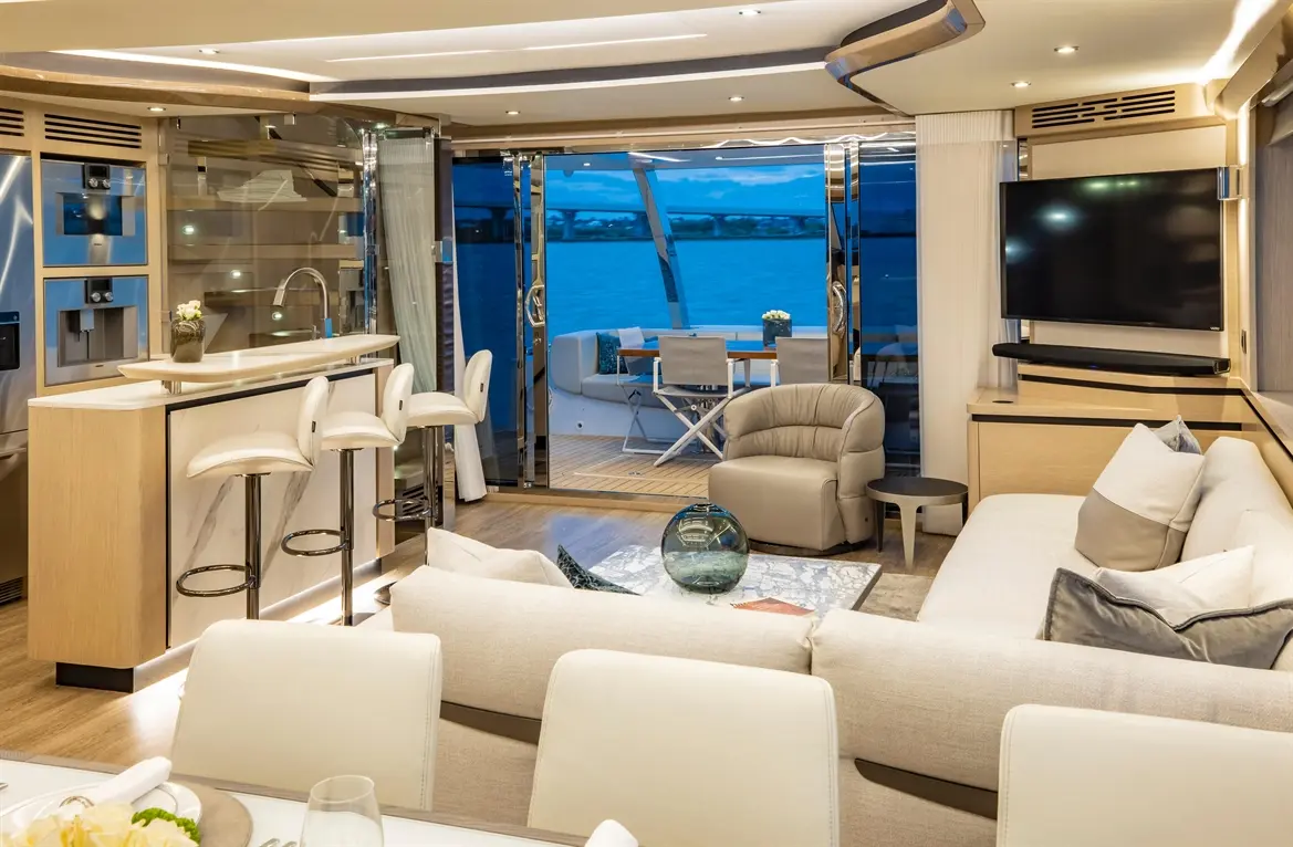 Luxurious yacht interior featuring a modern lounge, kitchen bar with stools, and views of the sea through large glass doors.